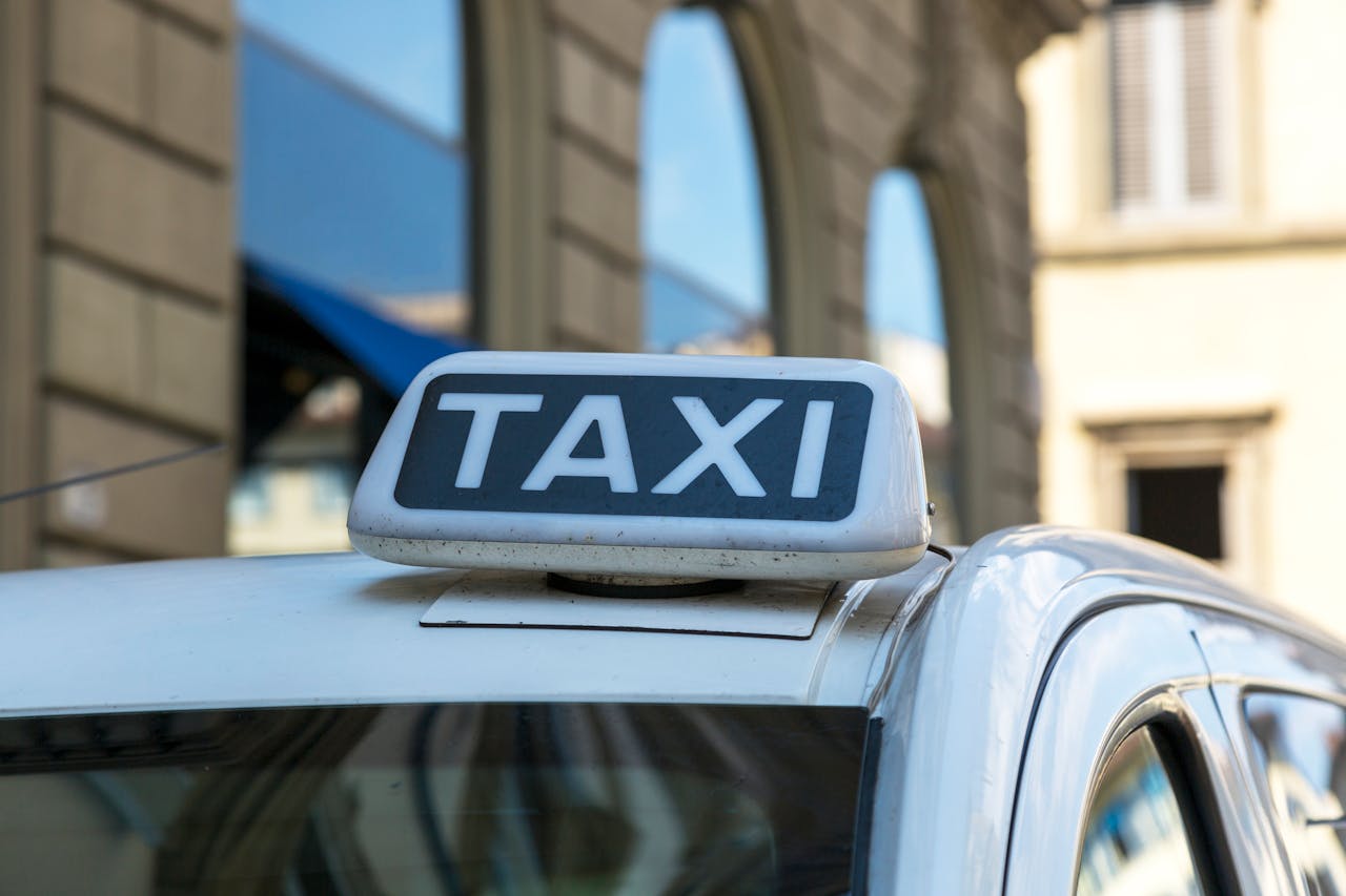 hero-img-01 Close-up view of a taxi sign atop a vehicle on an urban city street with blurred architectural background.